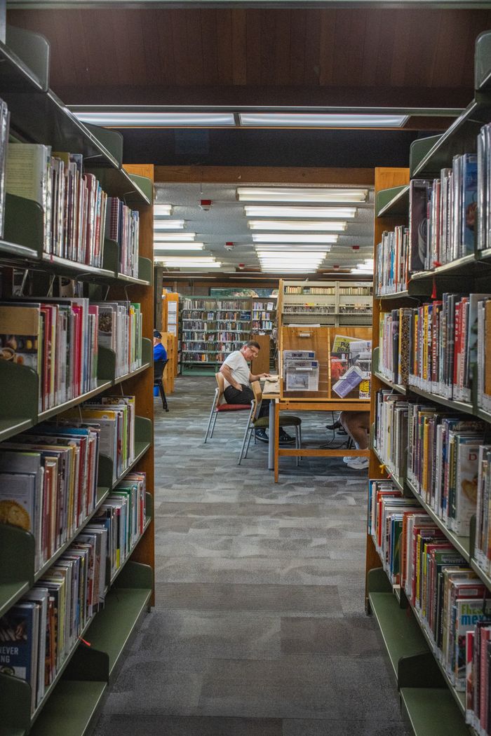 Adults studying in a cozy library aisle, surrounded by bookshelves. Ideal for education and reading concepts.