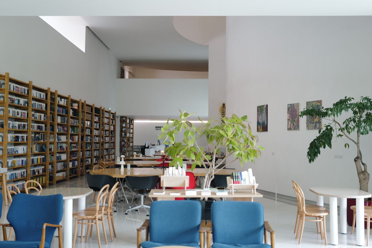 A spacious library interior showcasing shelves full of books, cozy seating, and indoor plants.